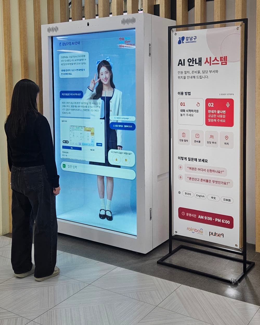 강남구청 1층 로비에 설치된 대화형 AR 홀로그램 박스 앞에서 방문객이 디지털 휴먼의 안내를 받는 모습